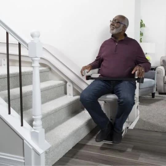Man riding a Bruno Elite curved stairlift on an indoor staircase